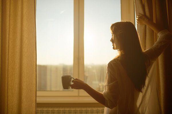 朝、カーテンを開けて陽の光を浴びる女性